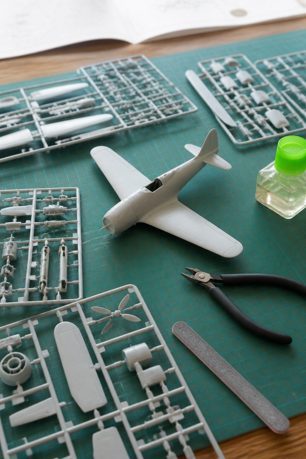 An unbuilt plastic model aircraft kit laid out on a cutting mat with sprue nippers, a sanding stick and a bottle of liquid cement