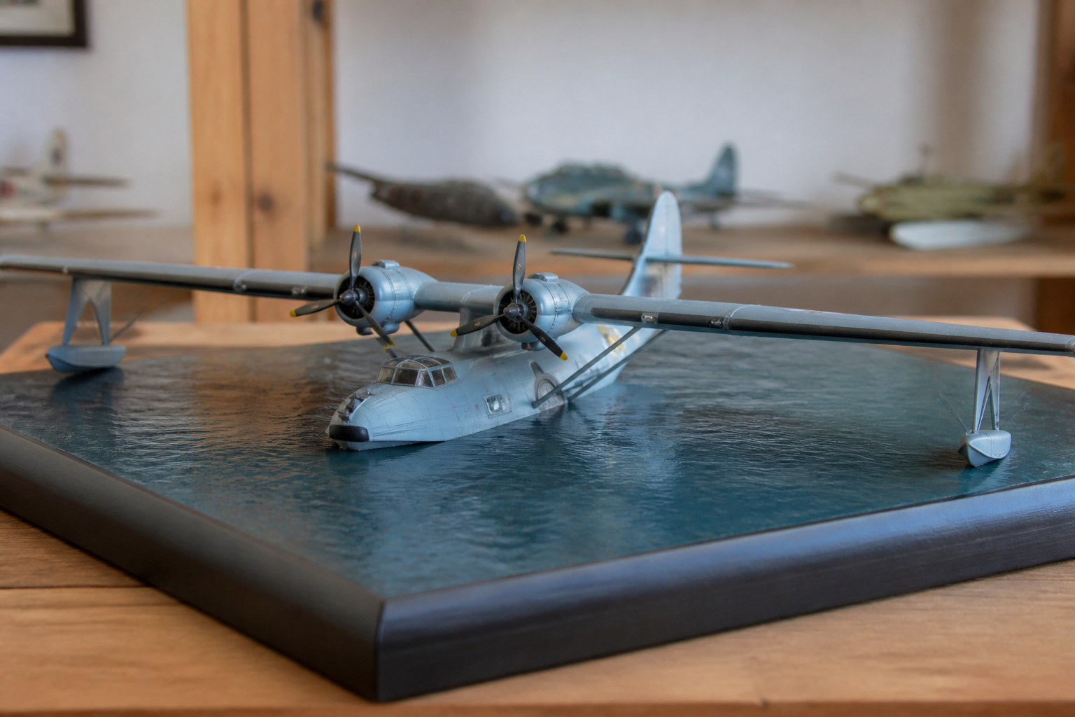 A twin-engine flying boat model with a boat hull and wingtip floats resting on a display base painted to suggest calm water