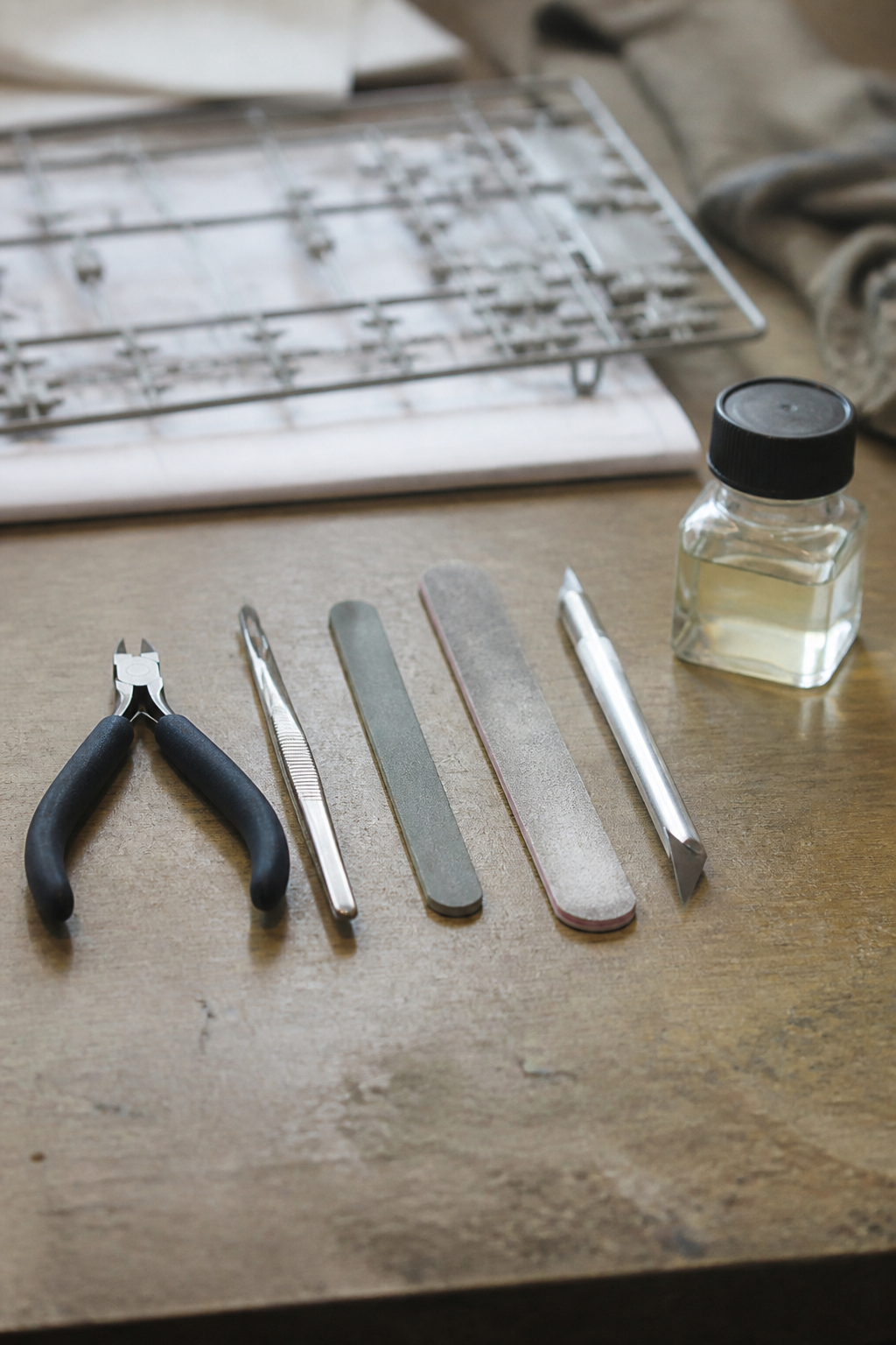 Modelling tools laid out in a row on a bench: sprue nippers, tweezers, sanding sticks, a scalpel and a pot of liquid cement